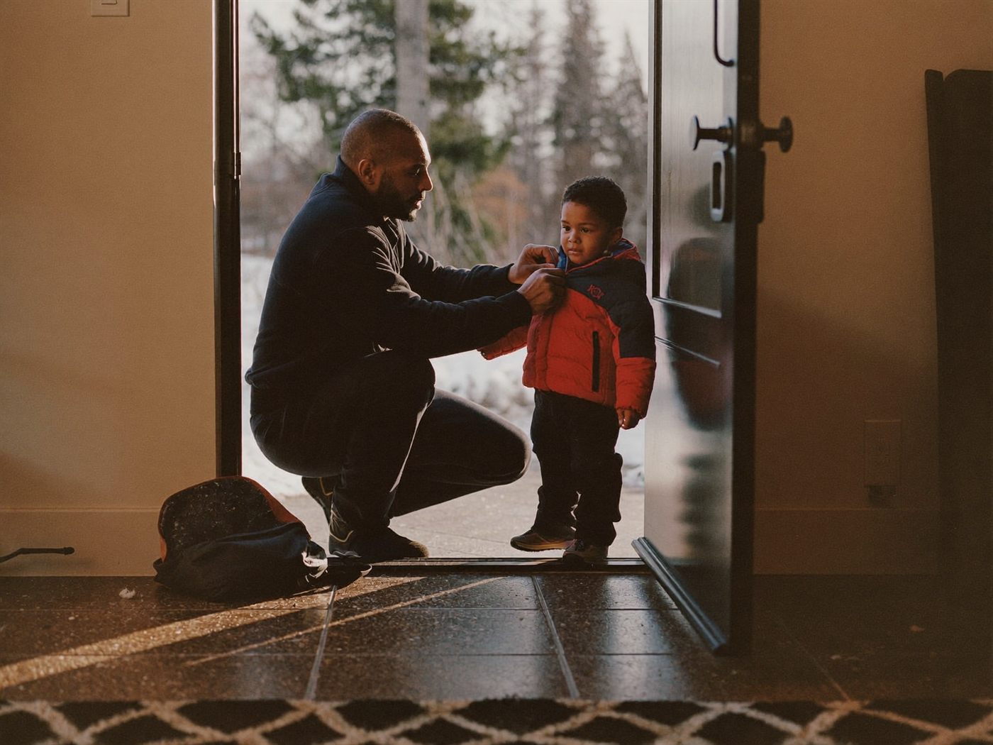 A father zipping up his young son's winter jacket on a snowy morning